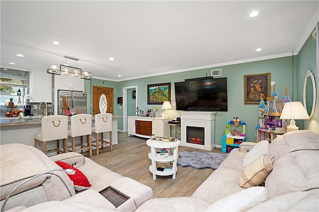 living room featuring crown molding, sink, and light hardwood / wood-style floors