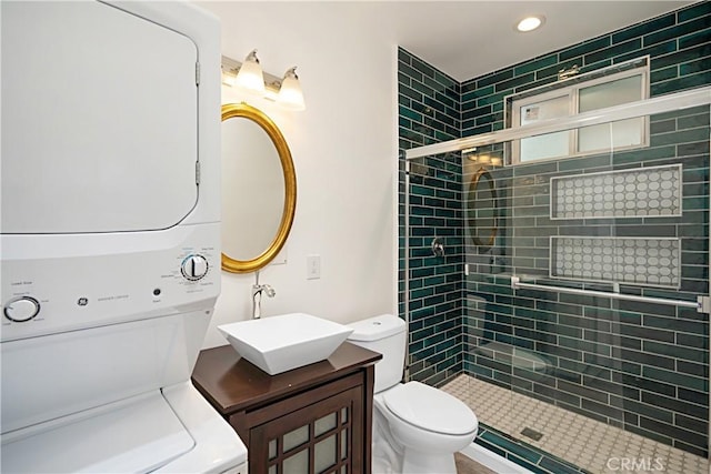 bathroom featuring toilet, tiled shower, vanity, and stacked washing maching and dryer