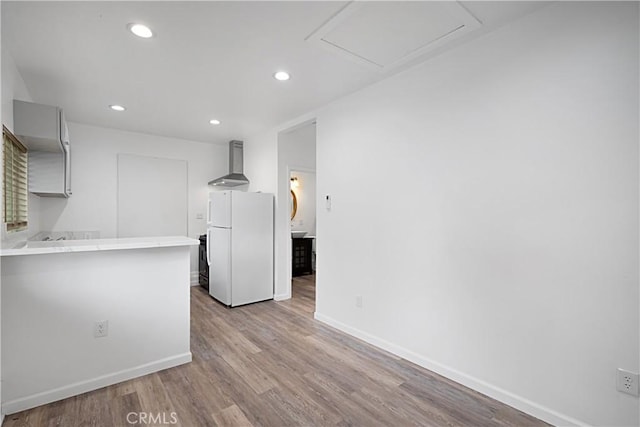 kitchen with light wood-type flooring, kitchen peninsula, wall chimney exhaust hood, and white fridge