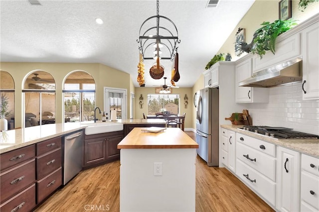 kitchen featuring stainless steel appliances, a kitchen island, wooden counters, range hood, and white cabinets