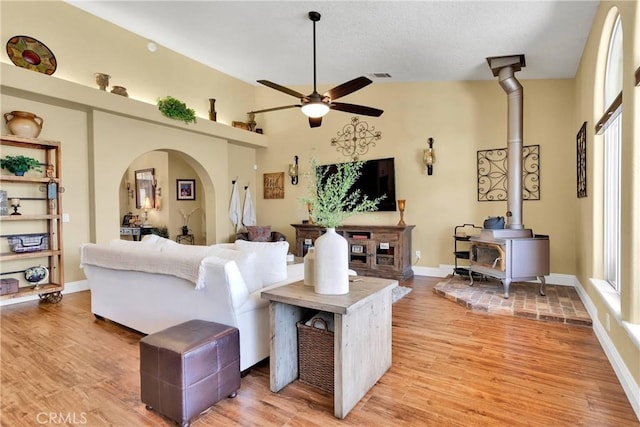 living room with light hardwood / wood-style floors, a wood stove, and ceiling fan