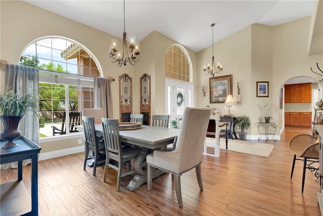 dining space with high vaulted ceiling, light wood-type flooring, and an inviting chandelier