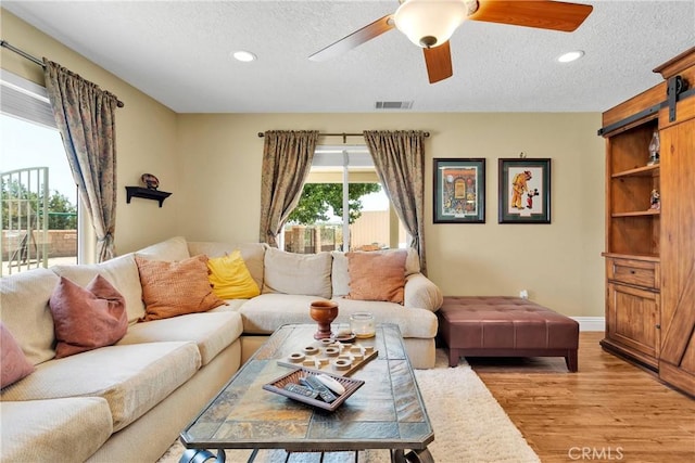 living room with light wood-type flooring, a textured ceiling, a barn door, and ceiling fan