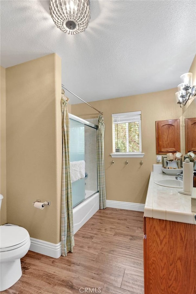 full bathroom featuring shower / bath combination with glass door, vanity, a textured ceiling, and toilet