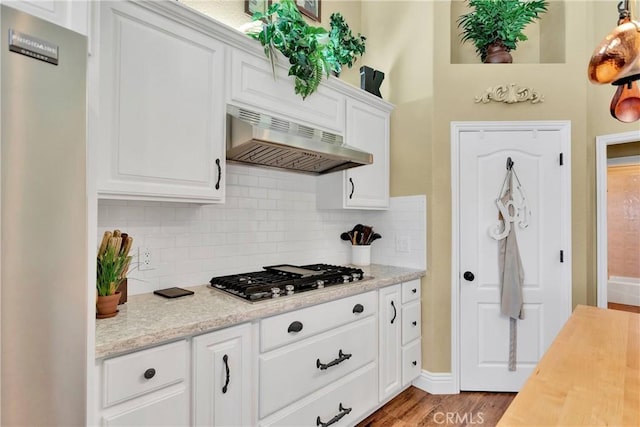 kitchen with ventilation hood, stainless steel gas stovetop, light hardwood / wood-style floors, and white cabinetry