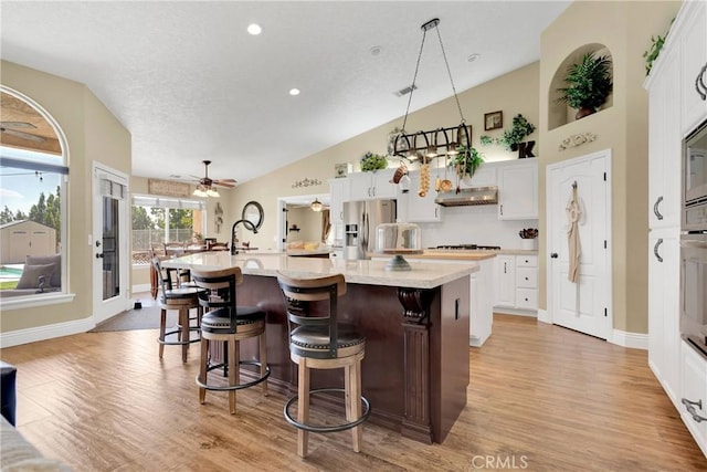 kitchen with stainless steel refrigerator with ice dispenser, a kitchen breakfast bar, pendant lighting, white cabinetry, and a large island