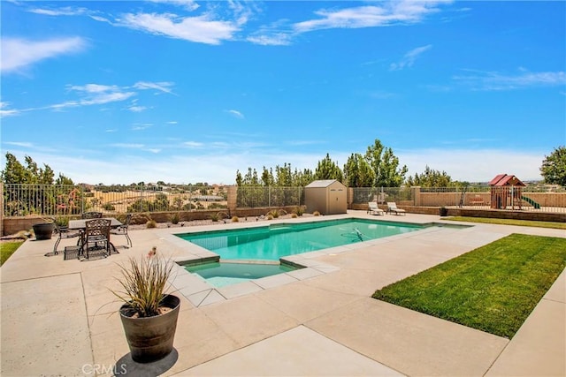 view of pool featuring an in ground hot tub, a playground, a patio area, and a storage shed