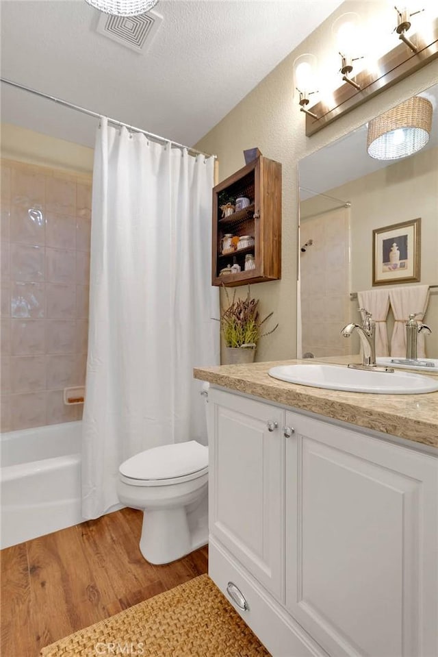 full bathroom with wood-type flooring, a textured ceiling, toilet, shower / bath combo with shower curtain, and vanity