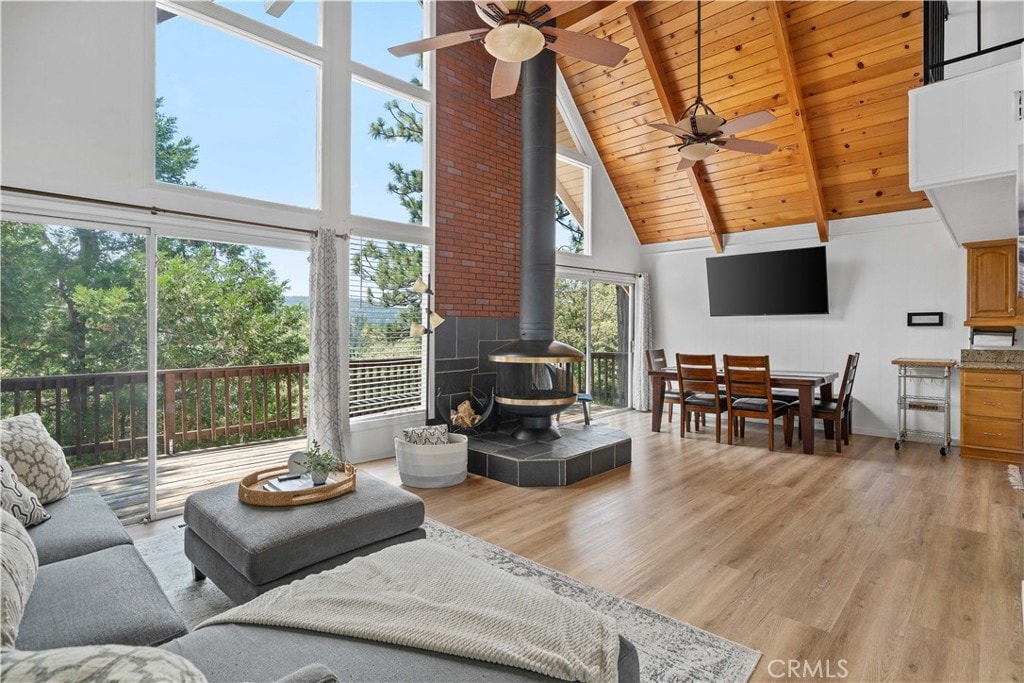 living area with high vaulted ceiling, a wood stove, wooden ceiling, and light wood-style flooring