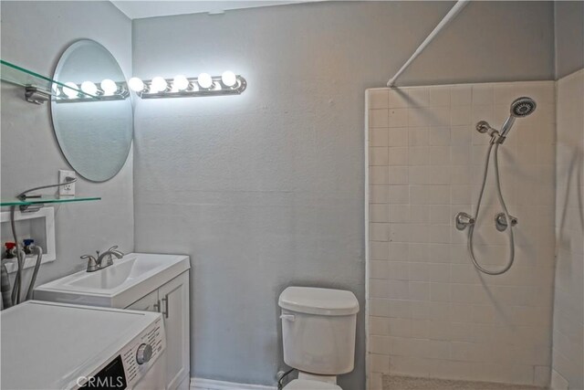 bathroom featuring toilet, washer / dryer, vanity, and a tile shower