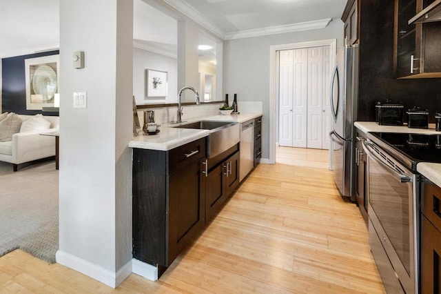 kitchen with sink, wall chimney range hood, appliances with stainless steel finishes, and dark brown cabinetry