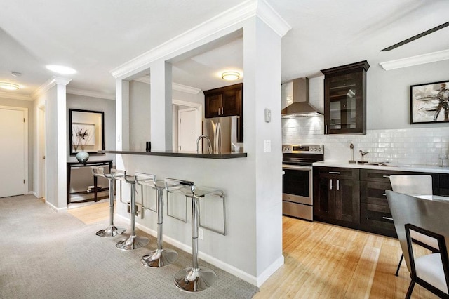 kitchen with crown molding, appliances with stainless steel finishes, backsplash, wall chimney range hood, and dark brown cabinetry