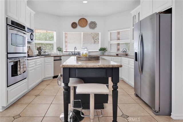 kitchen featuring a center island, stainless steel appliances, light tile patterned floors, and white cabinetry