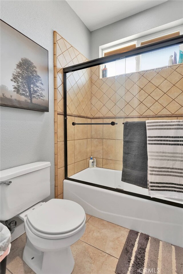 bathroom with tile patterned floors, toilet, and combined bath / shower with glass door