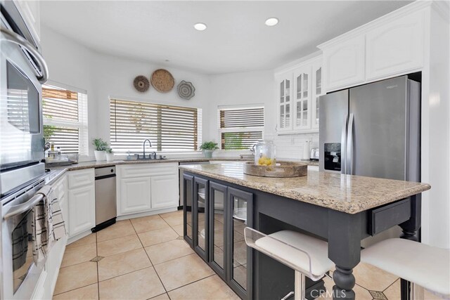 kitchen featuring white cabinets, appliances with stainless steel finishes, a wealth of natural light, and light stone counters