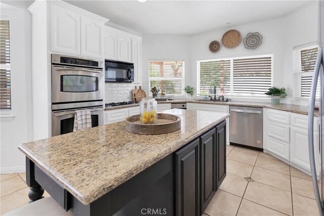 kitchen featuring light tile patterned floors, appliances with stainless steel finishes, light stone countertops, sink, and a kitchen island