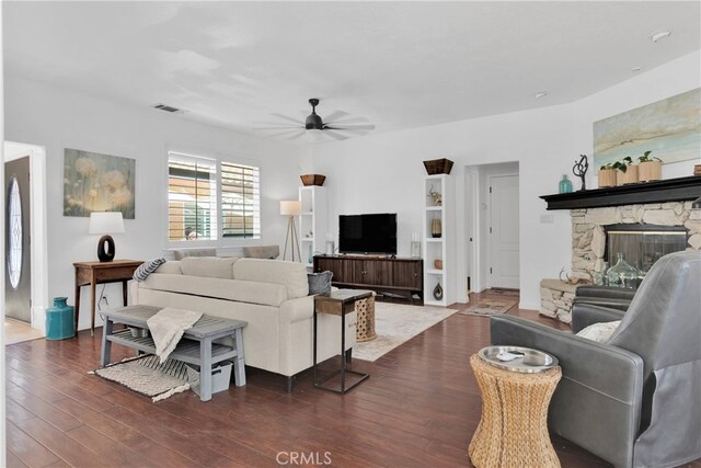 living room with dark wood-type flooring, ceiling fan, and a stone fireplace