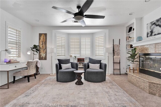 sitting room with built in features, light colored carpet, ceiling fan, and a textured ceiling