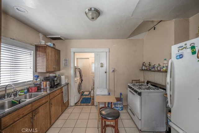 kitchen with a sink, white appliances, brown cabinetry, washer / clothes dryer, and light tile patterned floors