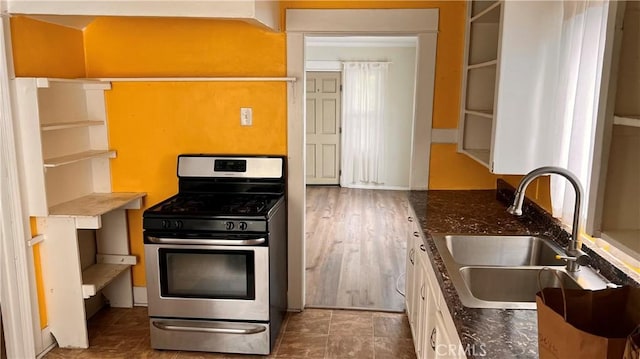 kitchen featuring open shelves, stainless steel range with gas cooktop, dark stone counters, white cabinets, and a sink