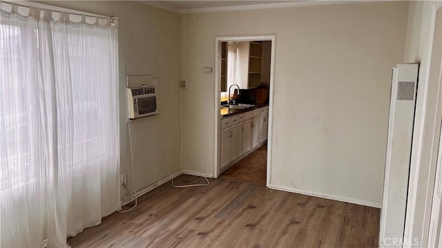 interior space with crown molding, a wall mounted AC, light wood-type flooring, a sink, and a heating unit