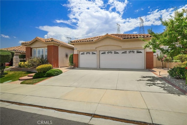 mediterranean / spanish home with an attached garage, driveway, a tile roof, and stucco siding