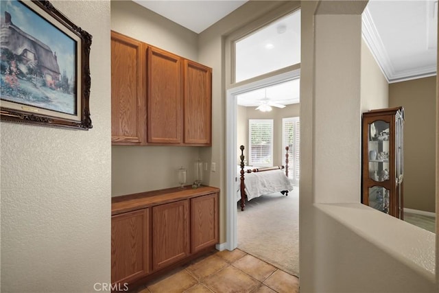 hall with light tile patterned floors, crown molding, and light colored carpet