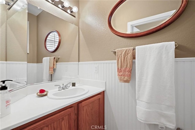 bathroom with a wainscoted wall, a textured wall, and vanity