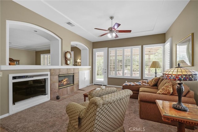 living room featuring ceiling fan, light carpet, visible vents, baseboards, and a tiled fireplace