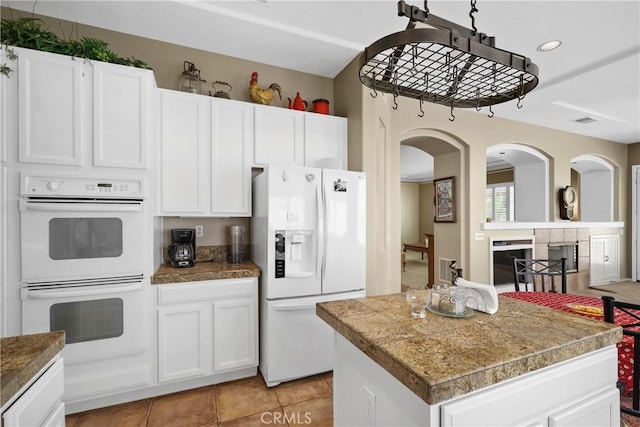 kitchen with white appliances, visible vents, white cabinets, tile countertops, and a kitchen island