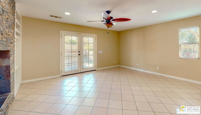 empty room with ceiling fan, light tile patterned floors, a fireplace, and french doors