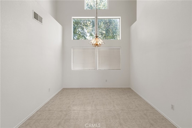 spare room with light tile patterned floors, an inviting chandelier, and a high ceiling