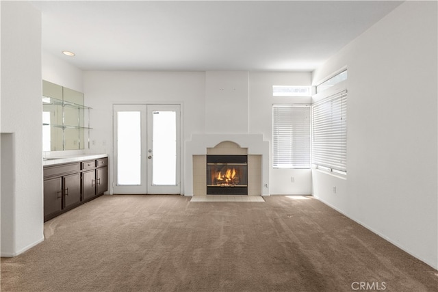 unfurnished living room with light carpet, a tiled fireplace, and a healthy amount of sunlight