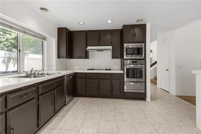 kitchen featuring light tile patterned floors, appliances with stainless steel finishes, dark brown cabinets, tile countertops, and sink