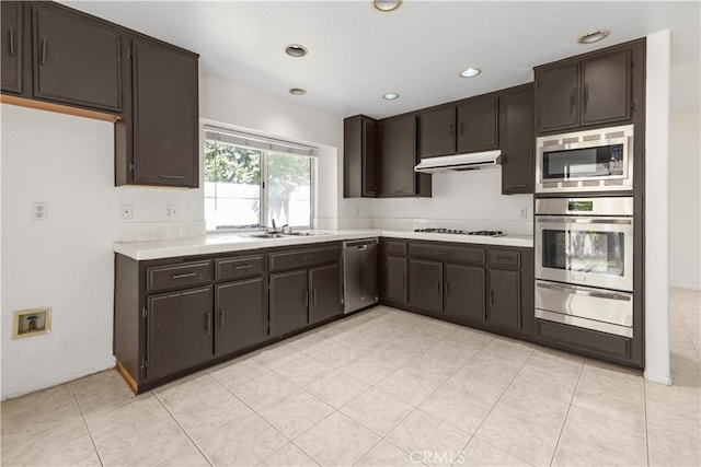 kitchen featuring appliances with stainless steel finishes, light tile patterned flooring, sink, and dark brown cabinetry