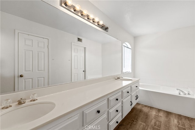 bathroom featuring a tub to relax in, dual bowl vanity, and hardwood / wood-style flooring