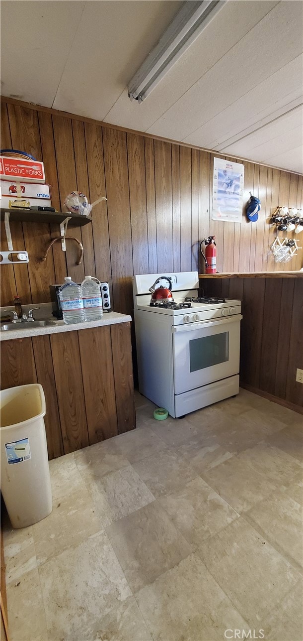 kitchen featuring white range with gas stovetop and wood walls