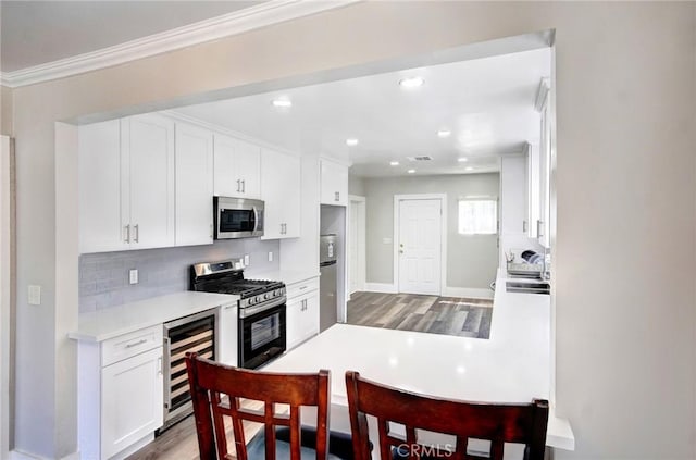 kitchen with wine cooler, stainless steel appliances, white cabinets, light countertops, and decorative backsplash