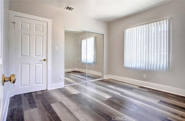 unfurnished bedroom featuring a closet, dark wood-style flooring, visible vents, and baseboards