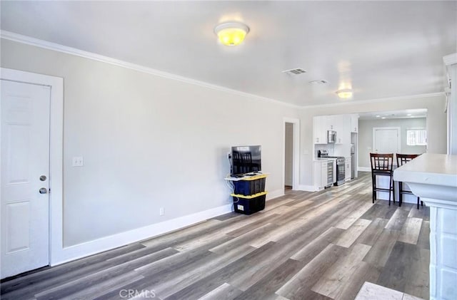 unfurnished living room with ornamental molding, visible vents, baseboards, and wood finished floors