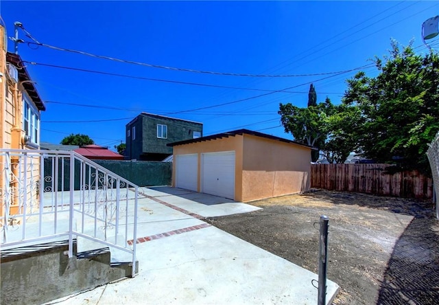 view of side of home with a detached garage, fence, an outbuilding, and stucco siding