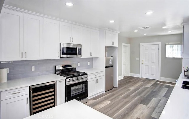 kitchen with beverage cooler, tasteful backsplash, white cabinets, stainless steel appliances, and light countertops