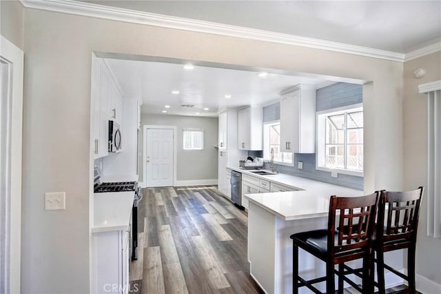 kitchen featuring white cabinets, appliances with stainless steel finishes, a peninsula, light countertops, and a kitchen bar