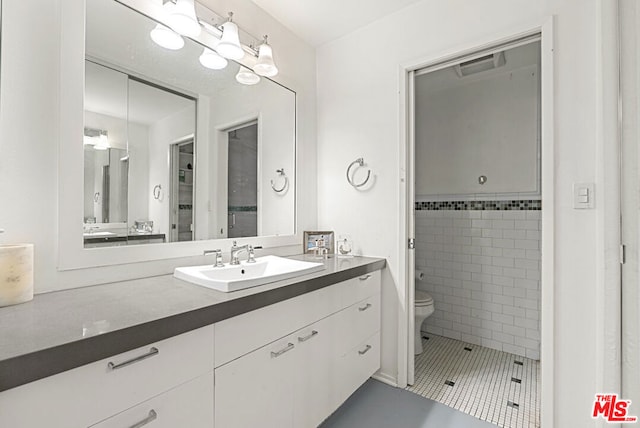 bathroom featuring toilet, a tile shower, vanity, and tile patterned floors