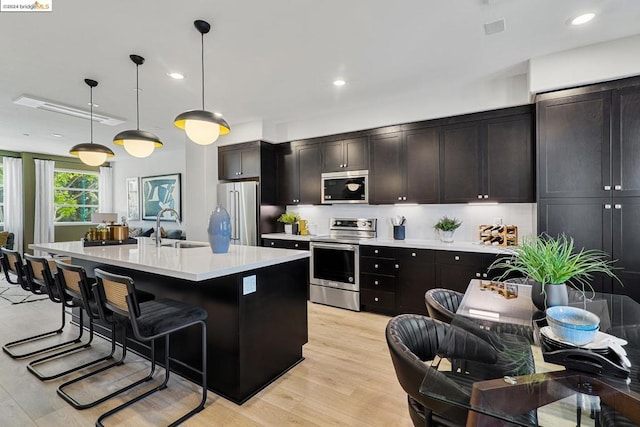 kitchen with sink, light wood-type flooring, pendant lighting, stainless steel appliances, and a kitchen island with sink