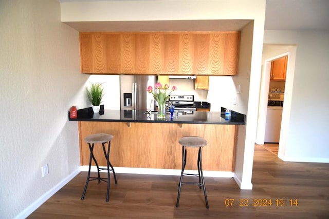 kitchen with dark hardwood / wood-style flooring, a breakfast bar area, stainless steel appliances, and kitchen peninsula