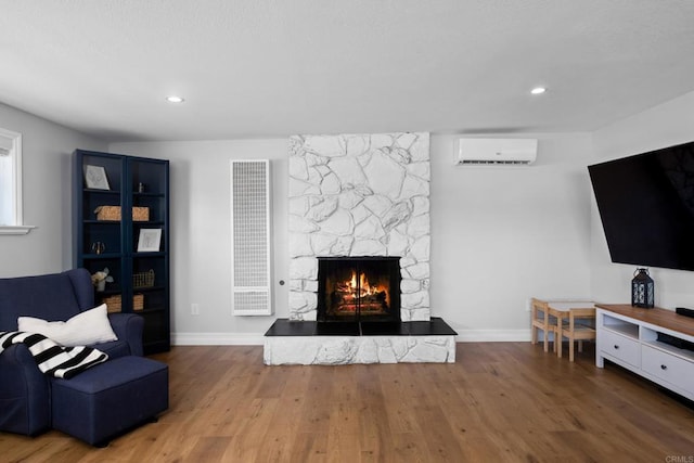 living room with a wall mounted AC, a stone fireplace, and wood-type flooring