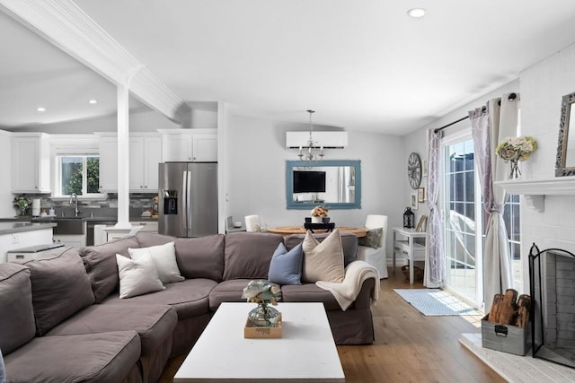 living room featuring an AC wall unit, light wood-type flooring, vaulted ceiling with beams, a notable chandelier, and a brick fireplace