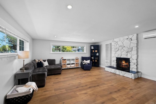 living room featuring a stone fireplace, hardwood / wood-style flooring, and a wall unit AC