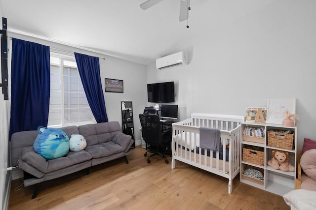 bedroom with light wood-type flooring, a wall mounted air conditioner, a nursery area, and ceiling fan